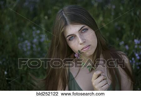 Stock Image - Portrait of pensive Caucasian woman holding flower. Fotosearch