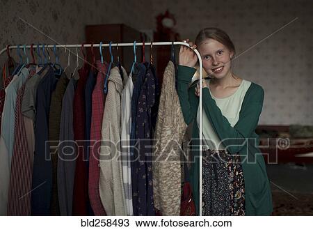 Stock Image - Portrait of pensive Caucasian woman leaning on clothing rack. Fotosearch