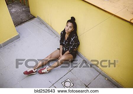 Stock Image - Portrait of serious African American woman sitting on sidewalk. Fotosearch
