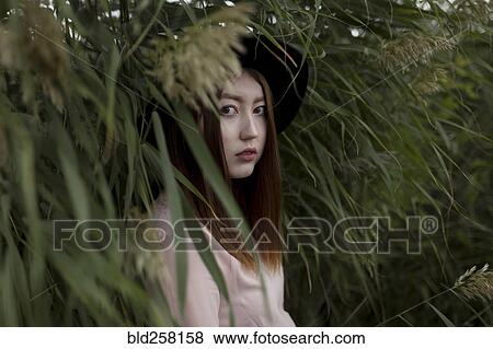 Stock Photo - Portrait of serious Asian woman standing in field of tall grass. Fotosearch