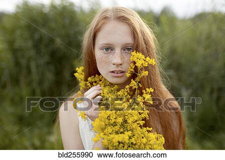 Stock Image - Portrait of serious Caucasian girl with freckles holding wildflowers. Fotosearch
