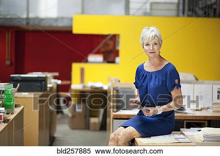 Stock Photography - Portrait of serious Caucasian businesswoman sitting on desk. Fotosearch