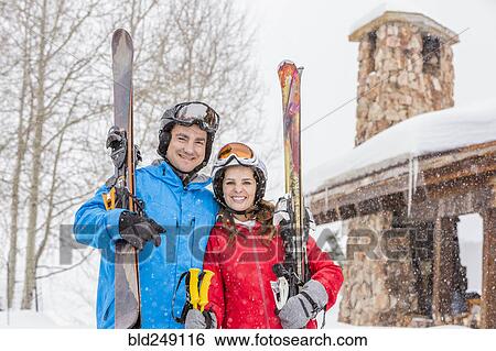 Stock Photograph - Portrait of smiling Caucasian couple carrying skis. Fotosearch