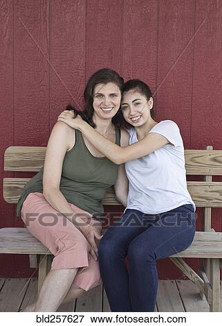 Stock Photo - Portrait of smiling Caucasian girl hugging mother on bench. Fotosearch