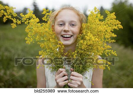 Stock Photo - Portrait of smiling Caucasian girl with freckles holding wildflowers. Fotosearch