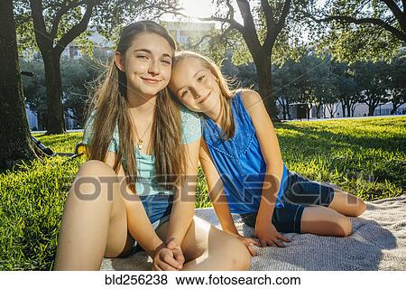 Stock Photo - Portrait of smiling Caucasian girls on blanket in park. Fotosearch