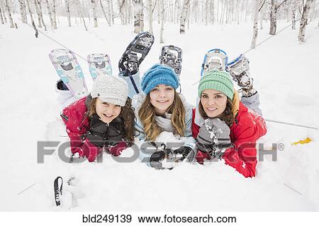 Stock Photo - Portrait of smiling Caucasian mother and daughters laying in snow. Fotosearch