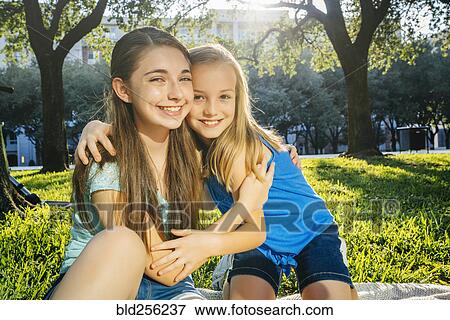 Stock Photo - Portrait of smiling Caucasian sisters hugging in park. Fotosearch