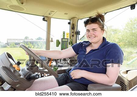 Stock Image - Portrait of smiling Caucasian woman driving tractor. Fotosearch