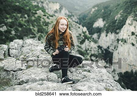 Portrait of smiling Caucasian woman sitting on rock holding camera View Large Photo Image Stock Image - Portrait of smiling Caucasian woman sitting on rock holding camera. Fotosearch