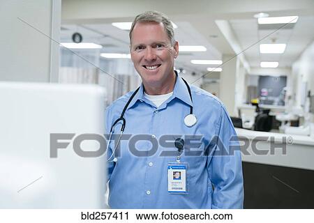 Stock Image - Portrait of smiling doctor using computer in hospital. Fotosearch