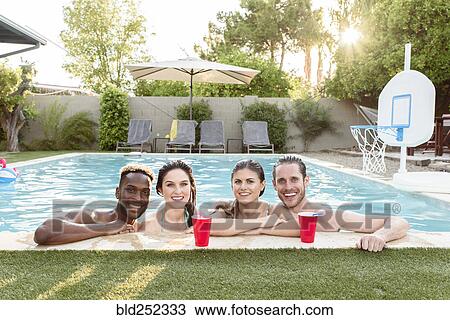 Stock Image - Portrait of smiling friends in swimming pool. Fotosearch
