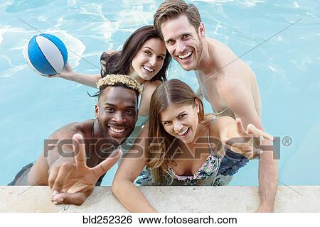 Stock Photograph - Portrait of smiling friends in swimming pool with basketball. Fotosearch