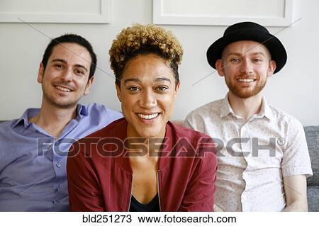 Stock Image - Portrait of smiling friends on sofa. Fotosearch