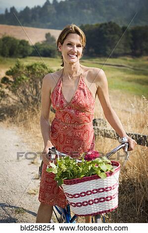 Picture - Portrait of smiling Hispanic woman riding bicycle with basket. Fotosearch
