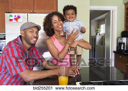 Stock Image - Portrait of smiling mixed race couple and baby son in kitchen. Fotosearch