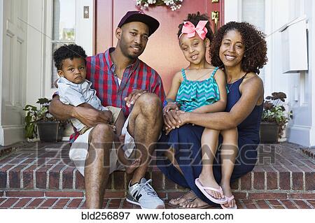 Stock Photo - Portrait of smiling mixed race family sitting on front stoop. Fotosearch