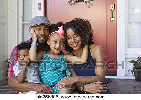 Stock Photo - Portrait of smiling mixed race family sitting on front stoop. Fotosearch