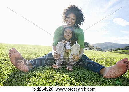 Stock Image - Portrait of smiling mixed race mother and daughter sitting in grass. Fotosearch