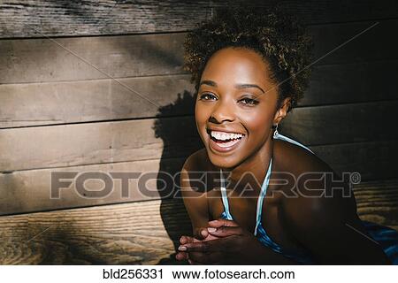 Stock Image - Portrait of smiling mixed race woman laughing near wooden wall. Fotosearch