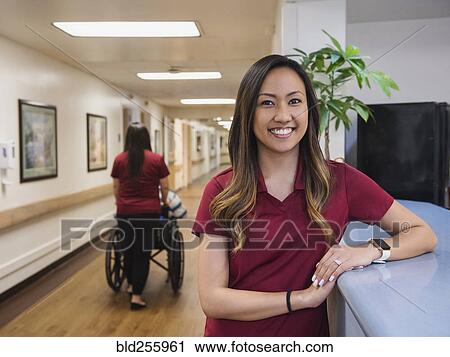 Stock Image - Portrait of smiling nurse leaning on counter in hospital. Fotosearch