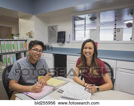 Stock Photograph - Portrait of smiling nurses writing in binders in hospital. Fotosearch