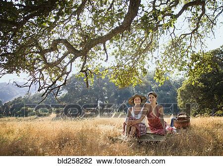 Stock Image - Portrait of smiling women relaxing on picnic blanket. Fotosearch