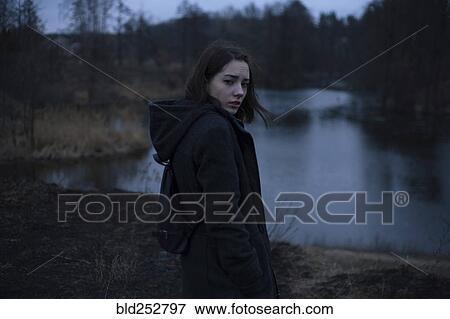 Stock Photo - Portraits of serious Caucasian woman standing near river at night. Fotosearch