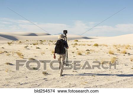 Picture - Rear view of Caucasian photographer carrying tripod in desert. Fotosearch
