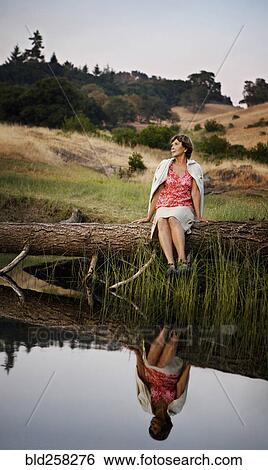 Reflection in lake of Caucasian woman sitting on log View Large Photo Image Stock Photograph - Reflection in lake of Caucasian woman sitting on log. Fotosearch