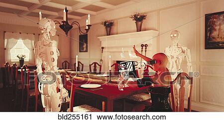 Stock Image - Robots watching woman at dining table wearing virtual reality goggles. Fotosearch