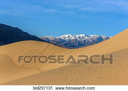 Stock Image - Sand dunes near snowy mountain range. Fotosearch