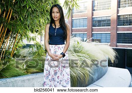 Stock Image - Serious Asian woman posing near foliage. Fotosearch