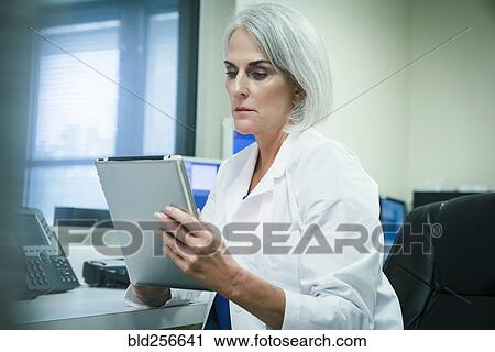Stock Image - Serious Caucasian doctor using digital tablet. Fotosearch