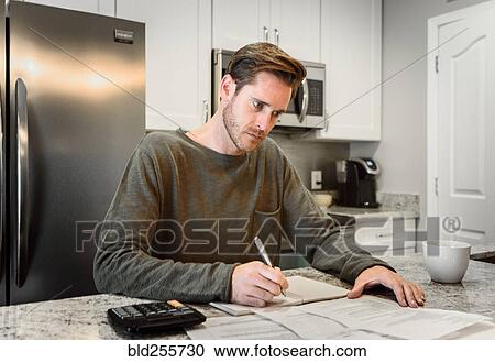 Stock Image - Serious Caucasian man writing notes and reading paperwork. Fotosearch