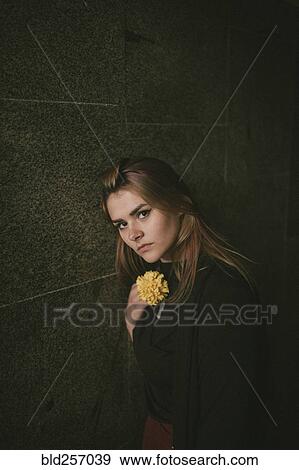 Serious Caucasian woman leaning on wall holding flower View Large Photo Image Stock Photo - Serious Caucasian woman leaning on wall holding flower. Fotosearch