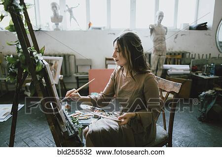Stock Image - Serious Caucasian woman painting on canvas. Fotosearch