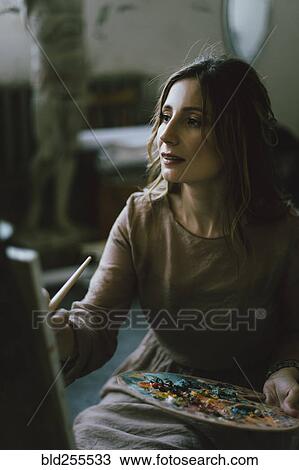 Stock Image - Serious Caucasian woman painting on canvas. Fotosearch