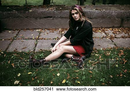 Stock Image - Serious Caucasian woman sitting in autumn leaves. Fotosearch