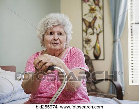 Serious Caucasian woman sitting on bed leaning on cane View Large Photo Image Picture - Serious Caucasian woman sitting on bed leaning on cane. Fotosearch