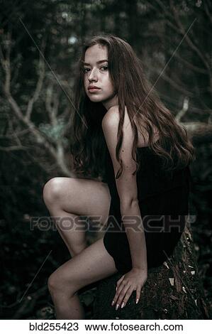 Stock Image - Serious Caucasian woman sitting on log in forest. Fotosearch