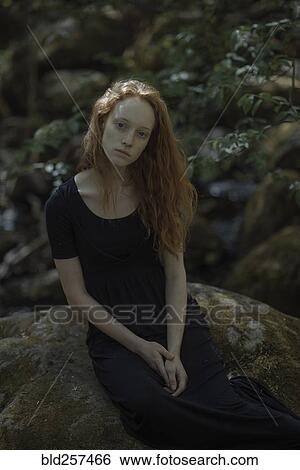Stock Photograph - Serious Caucasian woman sitting on rock. Fotosearch