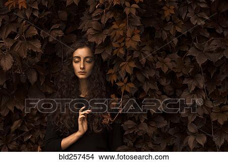 Picture - Serious Caucasian woman standing in autumn leaves. Fotosearch