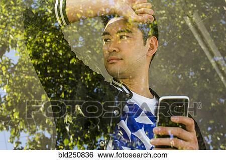 Stock Photograph - Serious Chinese man leaning on window holding cell phone. Fotosearch