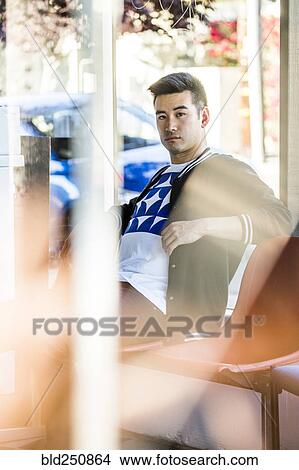 Picture - Serious Chinese man sitting in chair near window. Fotosearch