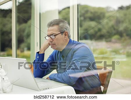 Stock Image - Serious Hispanic businessman using laptop. Fotosearch