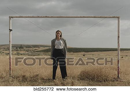Stock Image - Serious location woman standing in worn soccer goal. Fotosearch