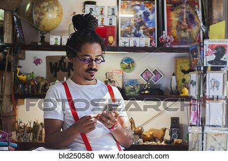Stock Image - Serious mixed race man wearing suspenders texting on cell phone. Fotosearch