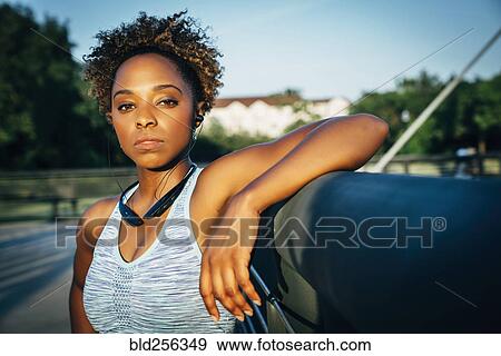 Stock Photo - Serious mixed race woman listening to earbuds on bridge. Fotosearch
