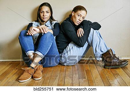 Stock Image - Serious mixed race women sitting on floor. Fotosearch